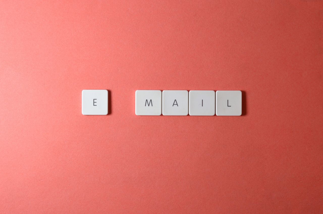 services-01 Flat lay of keyboard letter tiles spelling email on coral backdrop.